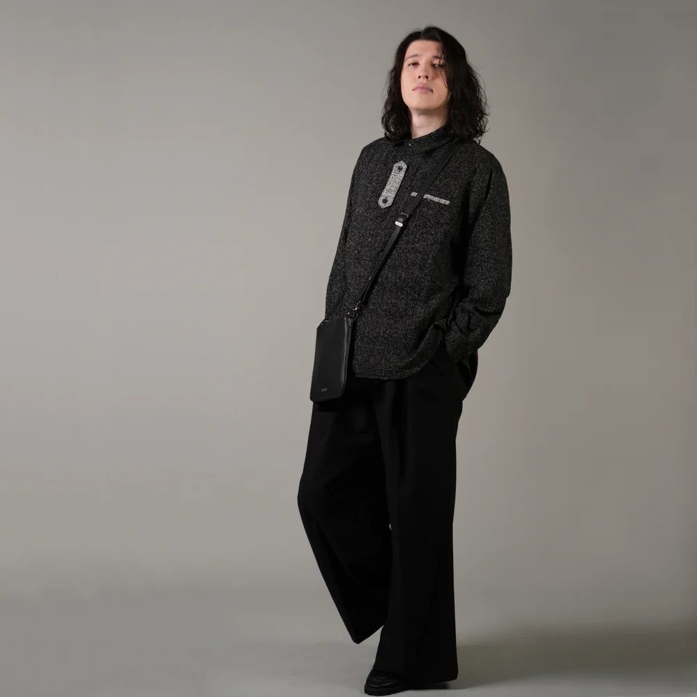 黒い服にショルダーバッグを掛けて立つ、長髪の男性